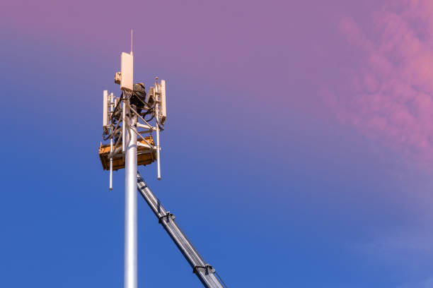 рабочие устанавливают сотовую базовую станцию с передатчиками 3g, 4g, 5g и антенны на вышки сотовой связи на фоне розово-голубого неба. мобильн - 3g стоковые фото и изображения