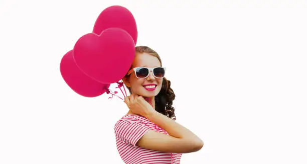 Young smiling woman holding a bunch of pink heart shaped balloons on a white background