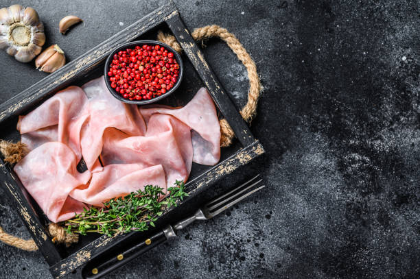 istock Thin sliced Smoked  pork ham in wooden tray. Black background. Top view. Copy space 1298163761