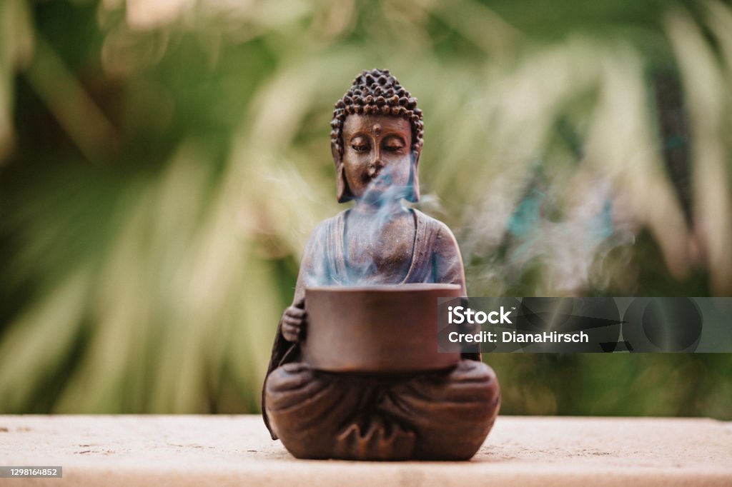 Buddha figurine with incense smoke on green background. Added grain. Incense Stock Photo