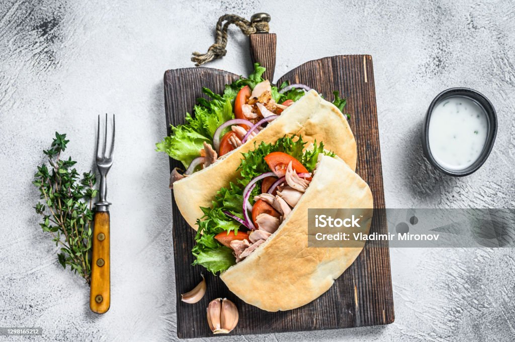 Pita sandwich with roasted chicken, vegetables and delicious sauce. White background. Top view Pita sandwich with roasted chicken, vegetables and delicious sauce. White background. Top view. Pita Bread Stock Photo