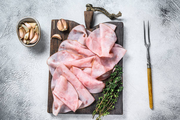 istock Ham Thin sliced on wooden cutting board with herbs. White background. Top view 1298165324