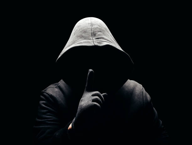 Horror man in hoodie showing silence hand sign in dark. stock photo