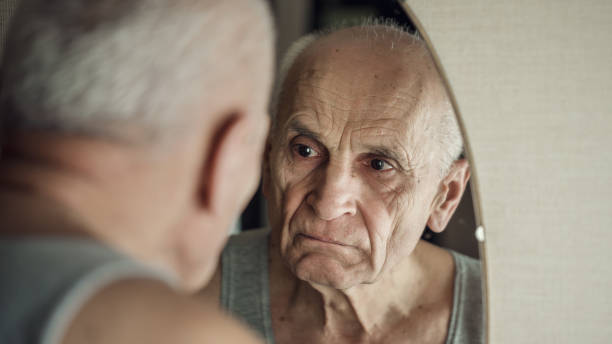istock Sullen aged gray haired man looks in mirror in his face reflection 1298168496