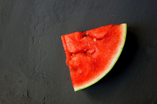 The watermelon is red on a black background. Summer concert. A slice of watermelon. Delicious berry. Flat lay, top view, copy space.