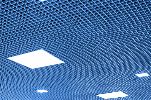 Mesh suspended ceiling with fluorescent or LED square lights in a modern shopping center or office building. Tinted