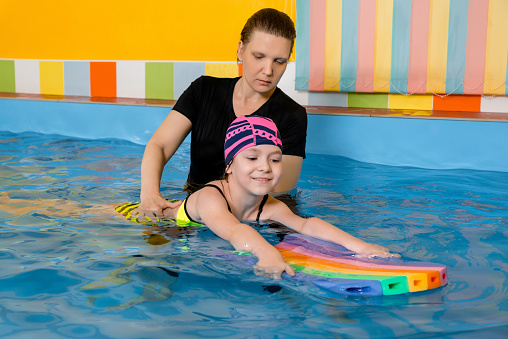 Coach teaching kid in indoor swimming pool how to swim and dive. Training concept