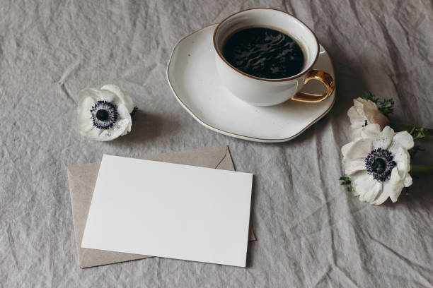 istock Spring wedding stationery mock-up scene. Blank greeting card, envelope on beige linen tablecloth background. White anemone flowers and cup of coffee. Feminine breakfast still life composition. 1298181097