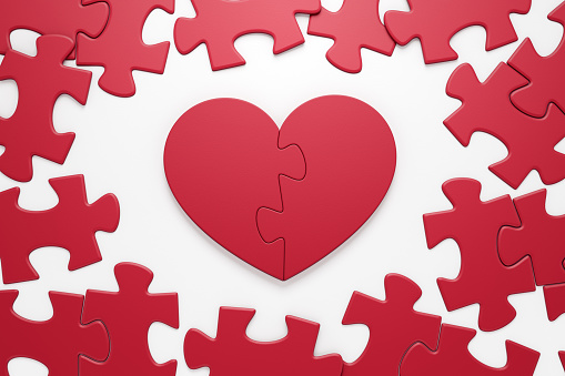 Jigsaw puzzle in form of a heart symbol composed from two halves  which are in center amongst the ordinary pieces of another jigsaw puzzle. 3D rendering graphics on the theme of Valentine's Day.
