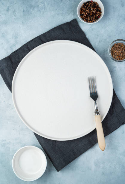 istock An empty flat white plate, fork, and spices in cups on a gray background 1298185841
