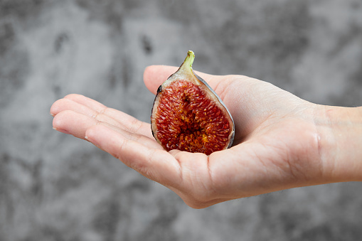 Hand holding a half slice of fig on marble background. High quality photo