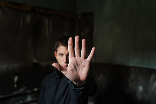 Close-up of a young man making a stop gesture with his palm. Focus on foreground