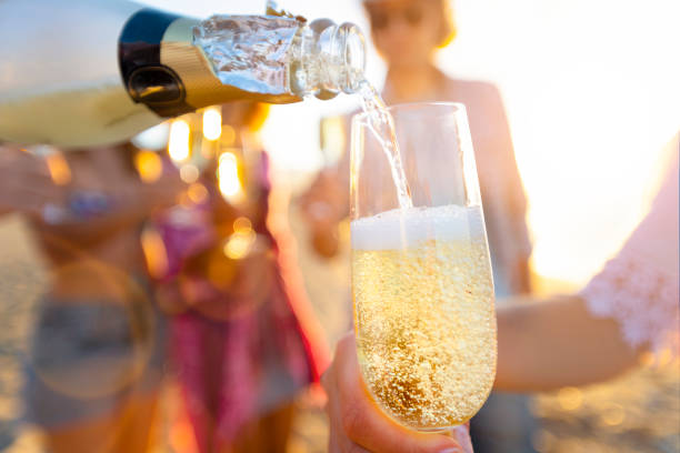 pouring a glass of champagne with people partying in the background. - champagne champagne flute pouring wine imagens e fotografias de stock