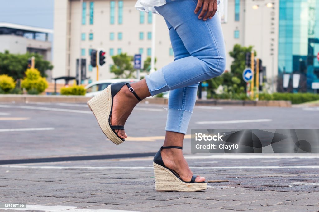 Woman In Blue Stylish Denim Jeans And Wedge Sandals With 1 Leg Raised In The City Street Stock Photo - Download Image - iStock