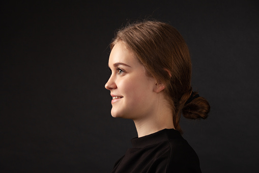 Close up studio portrait of 18 year old woman with brown hair in black clothes on black background
