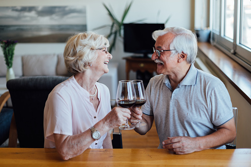 Happy Caucasian senior couple having fun at home, enjoying a glass of red wine and celebrating their marriage