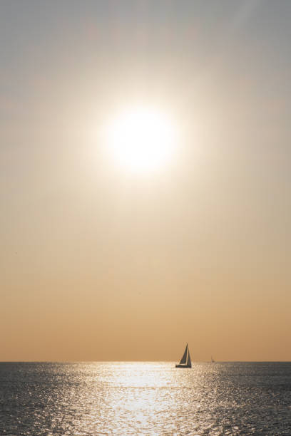 Orange colored seascape with sailboat over sunset sky