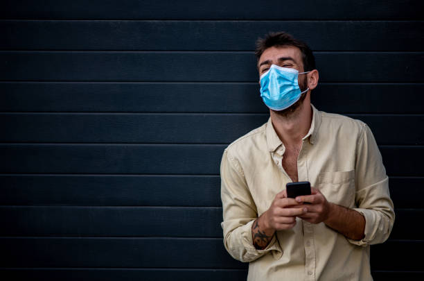 istock Isolated. Black background. Copy space. Young man with protective face mask is typing a message. 1298194350
