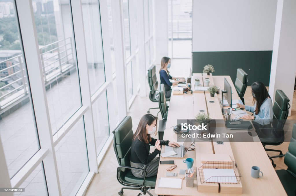 asian chinese beautiful women with protective facemask working in open plan office observing with new SOP and social distancing illness prevention safety precautions Office Stock Photo