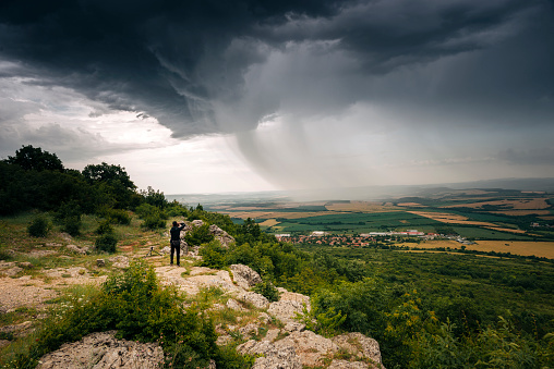 Man standing on the edge of the cliff and photograph a nice structured storm clouds in the summer fields