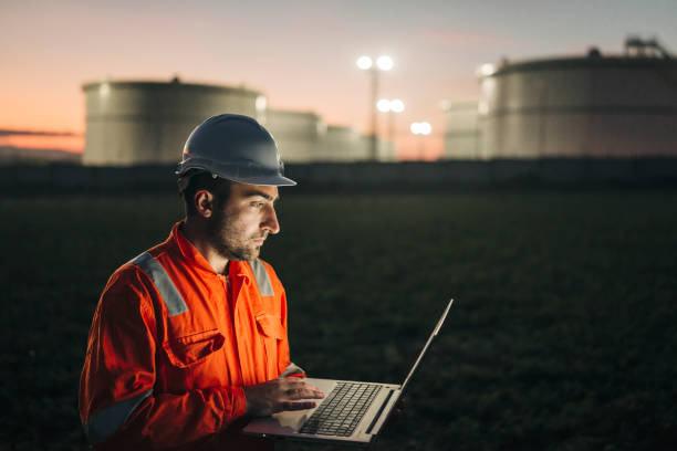 ingenieur mit laptop in der nähe von ölraffinerie in der nacht - petrochemical plant stock-fotos und bilder