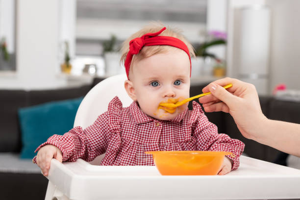 istock Mother Feeding Baby Sitting In Chair 1298200033