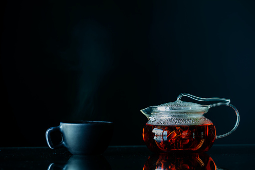 hot aromatic herbal tea with steam and reflection on black glass floor in dark background. Shot with high megapixel dslr camera, canon 5dsr