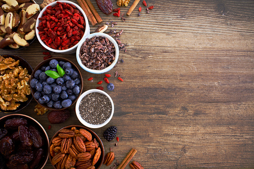 A selection of organic superfoods, nuts and fruit including blueberries, walnuts, goji berries, chia seeds, pecans and cacao nibs.
Shot from above on rustic wooden background with copy space to the right of the image. 
Healthy foods concept/ flat lay.