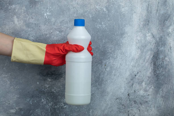 Hand in red gloves holding container of bleach Hand in red gloves holding container of bleach. High quality photo bleach stock pictures, royalty-free photos & images