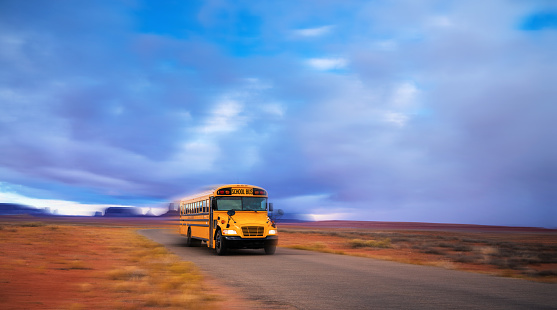 Yellow school bus driving early in the morning on Monument valley Arizona USA