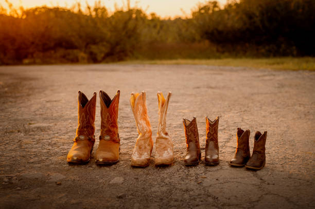 Cowboy boots for mom, dad, and two little children lined up on a dirt road at golden hour