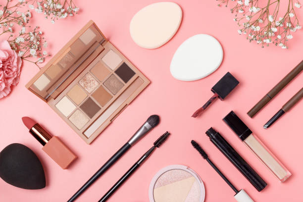 Decorative cosmetics and flowers on pink background top view.