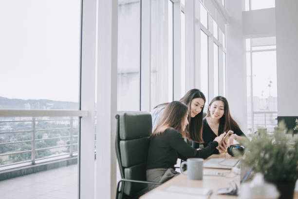 3 asian chinese white collar women having discussion in open plan office looking at smart phone  smiling 3 asian chinese white collar women having discussion in open plan office looking at smart phone gossip photos stock pictures, royalty-free photos & images