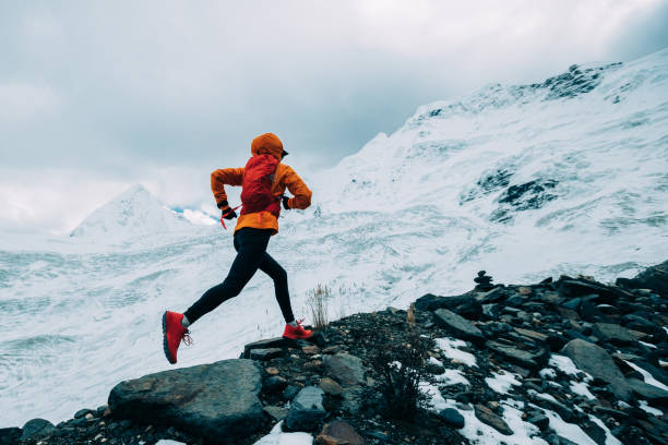 Woman trail runner cross country running up to winter snow mountain top stock photo