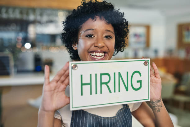 Work for us, we're hiring! Portrait of a young woman holding a "hiring" sign in her store help wanted sign photos stock pictures, royalty-free photos & images