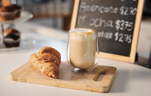 Closeup shot of a croissant and a cup of coffee on a wooden serving board in a cafe