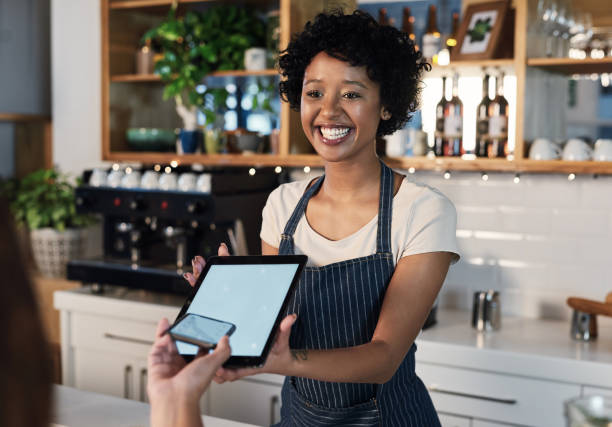 Providing top service, from the cash register to the kitchen Shot of a young woman accepting a digital payment from a customer in a cafe point of sale stock pictures, royalty-free photos & images