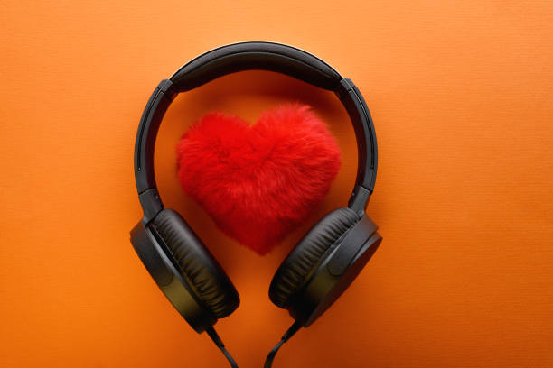 corazón rojo y auriculares negros sobre un fondo naranja. me encanta el concepto de estilo de vida musical. día de san valentín - romantic sky audio fotografías e imágenes de stock