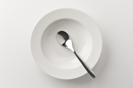 A white plate on a white table with a spoon There is no food on the plate. Household equipment