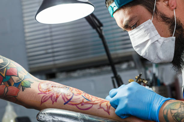 tatuatore con la sua macchina tatuaggio sul braccio con il disegno disegnato - tatuare foto e immagini stock