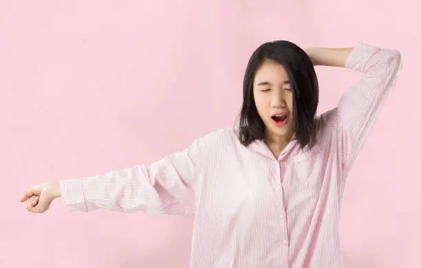 young asian woman wear pink pajamas yawn and stretch when her wake up feeling sleepy