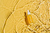 Bottle serum with vitamin C, cosmetic in clean transparent water with sunlight on yellow background