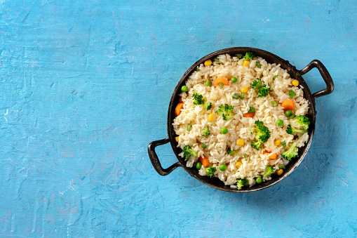 Vegetable rice with broccoli, green peas and carrots, shot from above on a blue background with a place for text