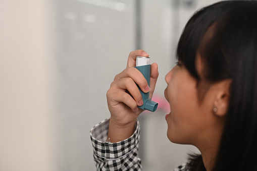 Asthmatic young girl using an asthma inhaler while suffering from asthma in toilet at home.