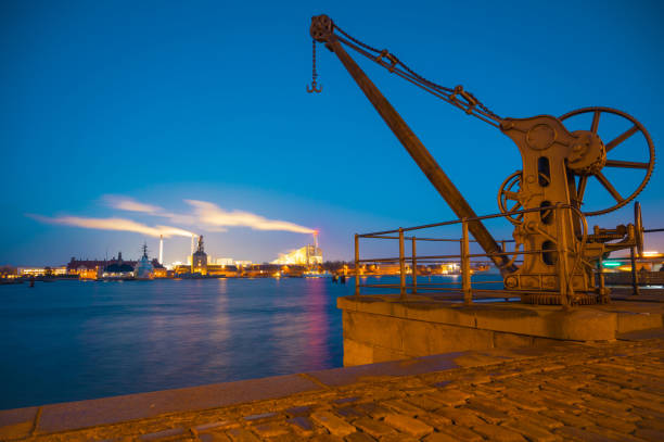 antigua grúa portuaria con el fondo de la fábrica de trabajo por la noche en copenhague, dinamarca. larsens plads amaliekaj, famoso muelle cerca de nyhavn. luces de exposición larga y cielo despejado con estrellas. antiguos edificios europeos - harbor night denmark crane fotografías e imágenes de stock