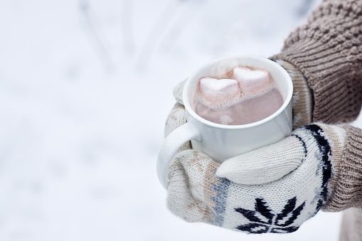 woman hands in mittens holding mug with hot cocoa outdoors. Winter and Valentine's day concept