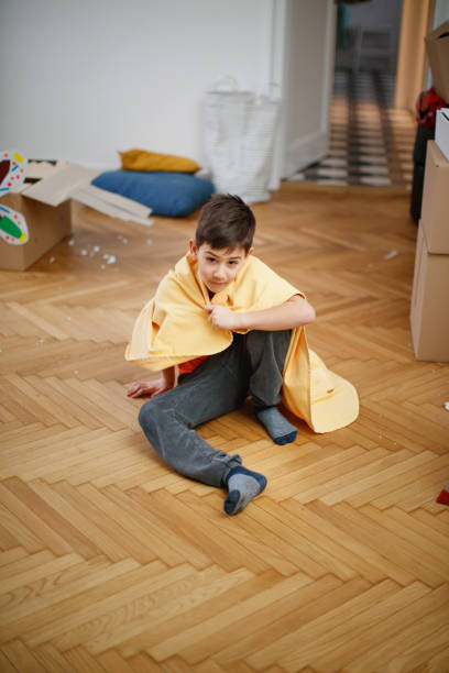 istock Boy sitting on floor with tablecloth over shoulders as cloak during house move 1298245374