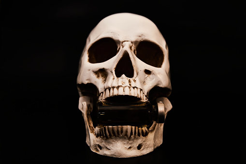 A glass vial in the jaw of a human skull model. Low-key photo.
