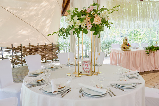 Table setting with white plate with napkin, cutlery and flowers on table, copy space. Place setting at wedding reception. Table served for banquet in restaurant