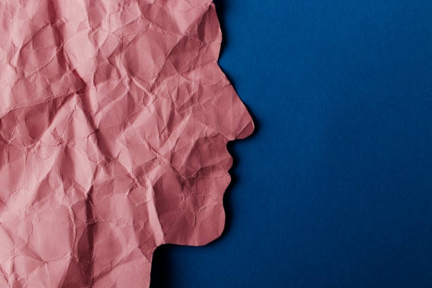 istock Crumpled pink paper shaped as a human head with copy space on blue paper background. 1298249095